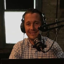 A photograph of Devon O'Reilly looking into the camera with headphones on and sitting in front of a microphone.