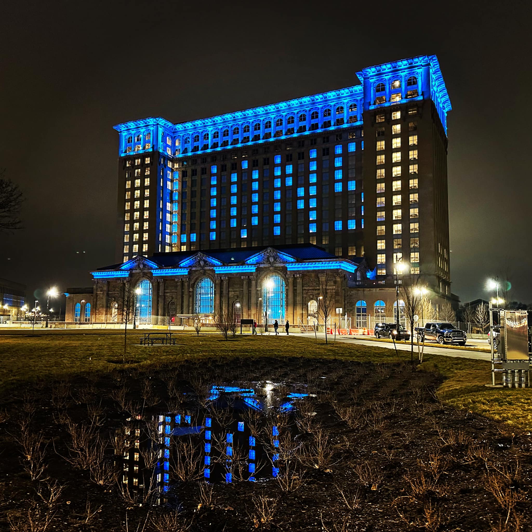 Photograph of the front of the renovated Michigan Central Building in Corktown, Detroit taken at night. The facade lighting in Detroit Lions Blue and the windows are lighted up to spell LIONS.